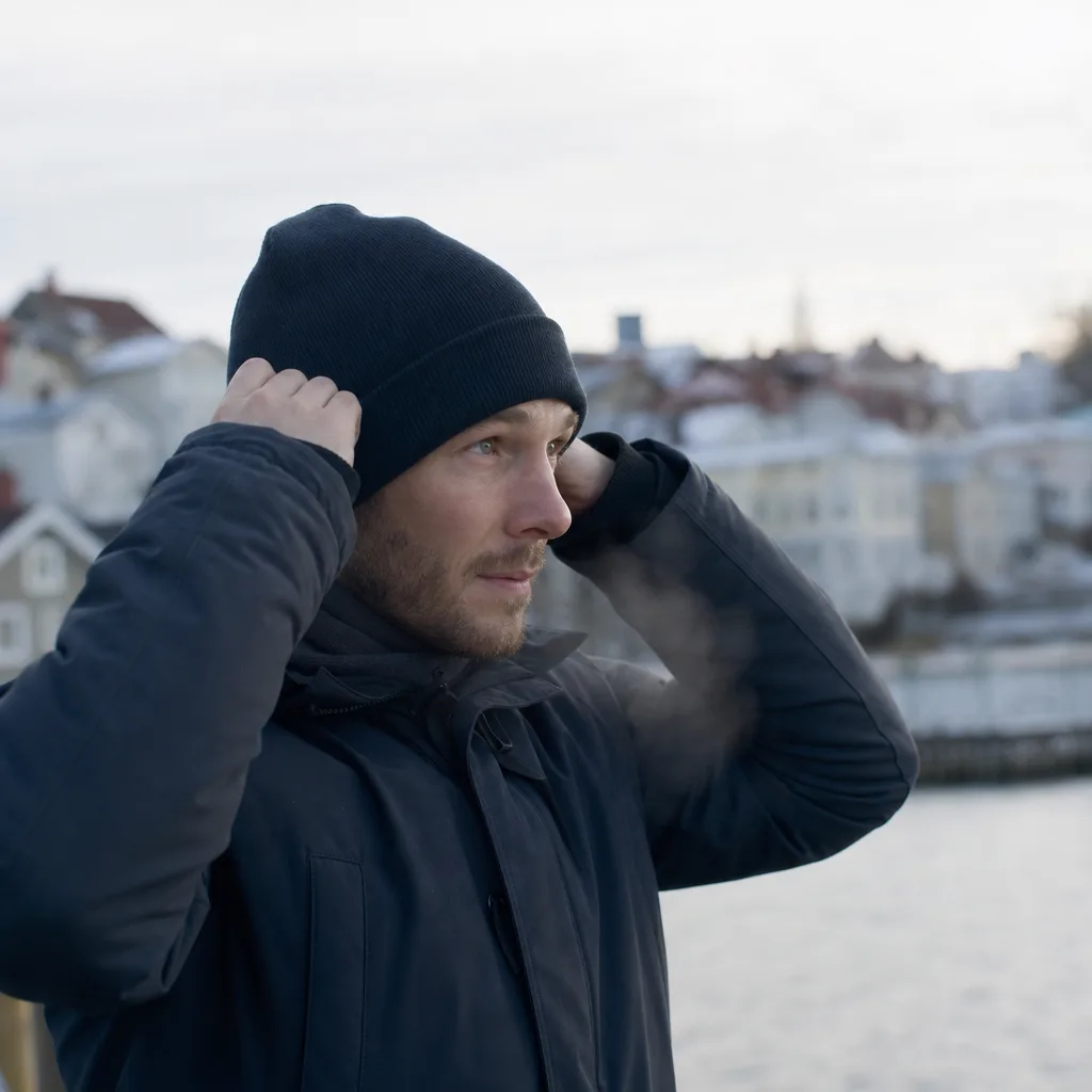Man drar på sig en mörk stickad mössa utomhus en kall dag